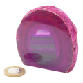 A polished magenta-purple agate geode showing concentric banding, displayed on a white background with a gold coin below for scale.