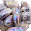 A pile of polished aura amethyst tumbled stones with a smooth, rounded shape and an iridescent sheen showing purple, blue, green, and gold reflections.