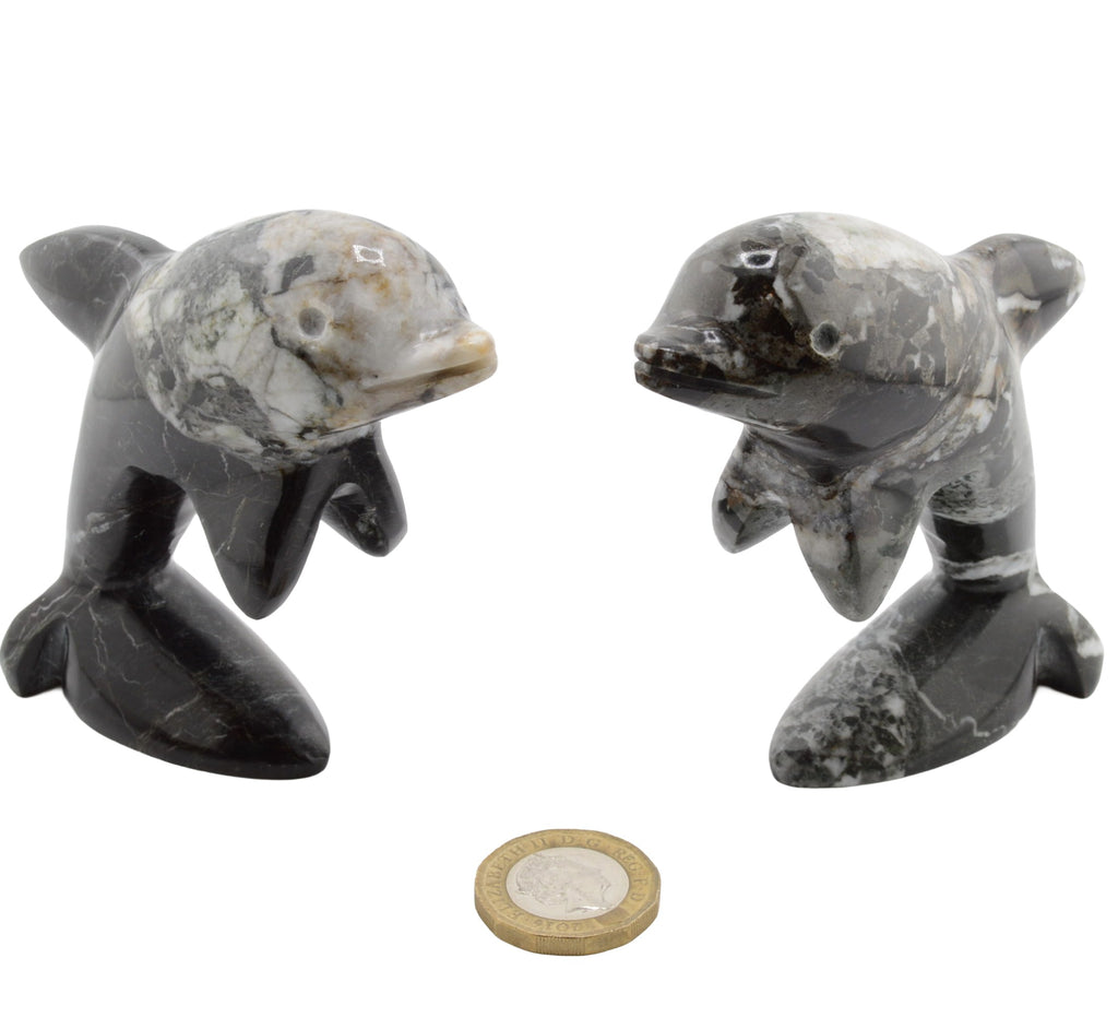 Two small polished stone dolphin figurines shown side by side on a white background, with a coin placed below for scale.