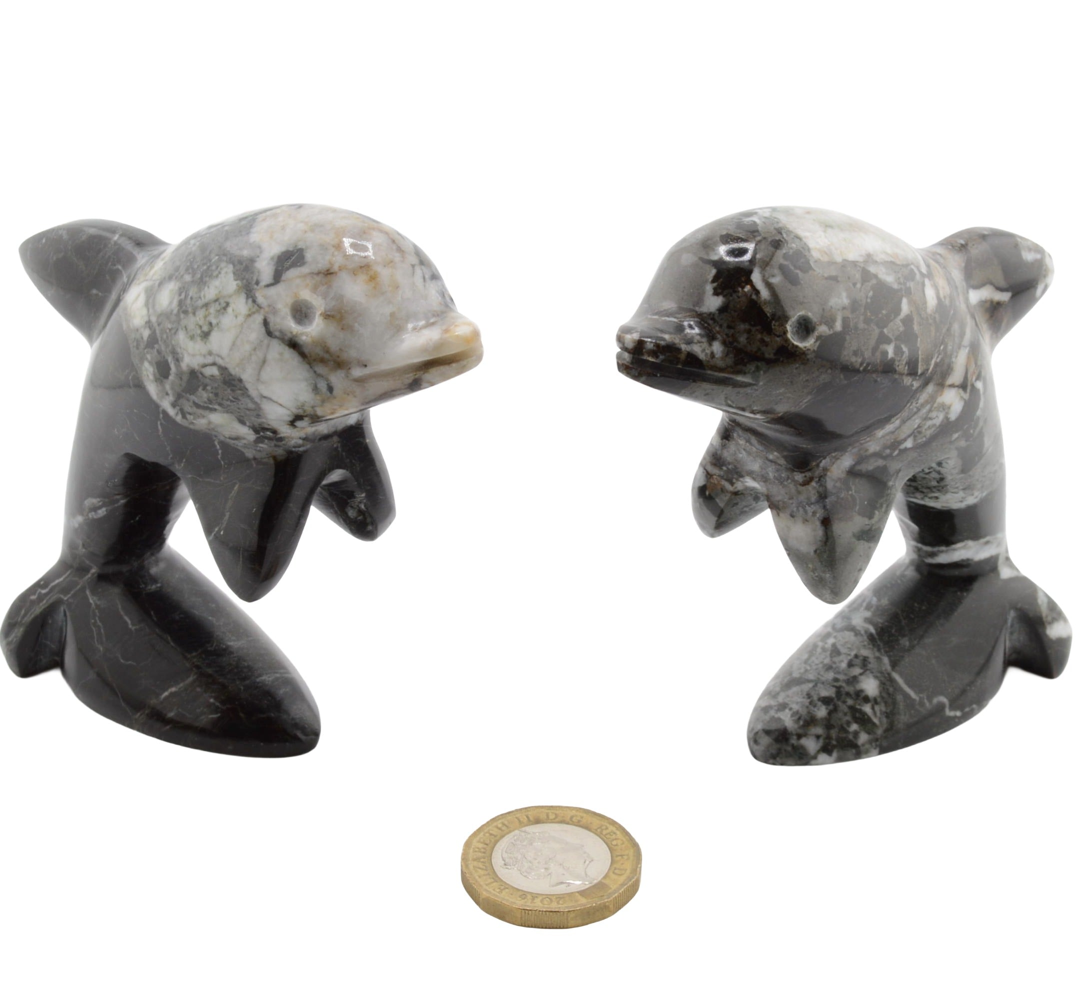 Two small polished stone dolphin figurines shown side by side on a white background, with a coin placed below for scale.